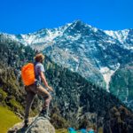 man-wearing-blue-shirt-standing-on-cliff-while-watching-2450296